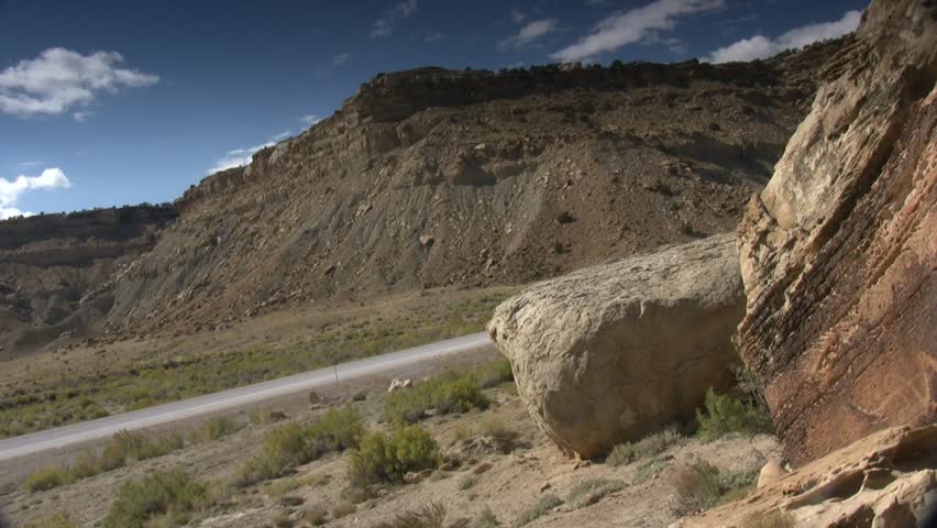 Wide shot; Pan right to snake petroglyph on large boulder, neutral grad sky.