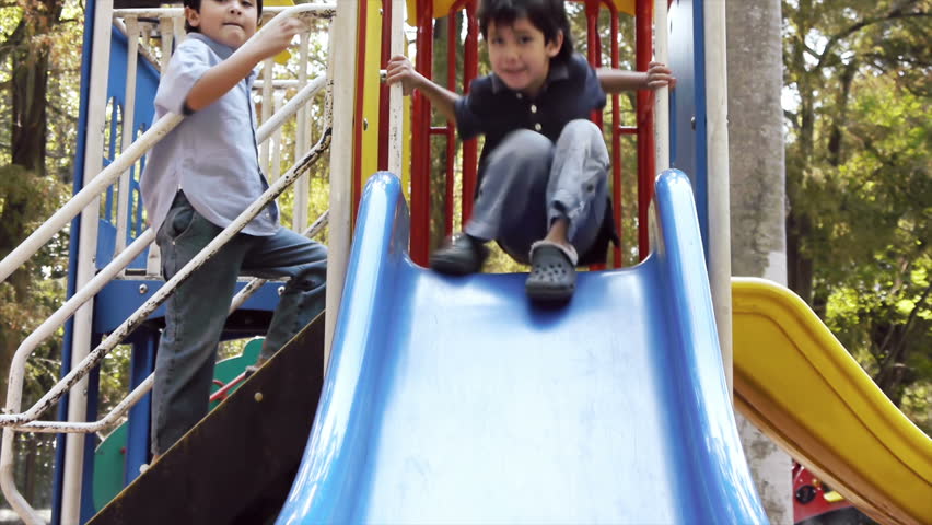 Two Latino Kid Brothers Playing on a Public Park Slide Seen from the Front.