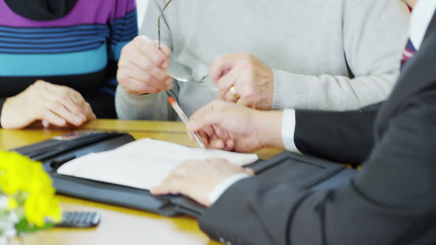 A senior couple meet with a financial adviser and sign up for an investment or policy of some kind. In slow motion.