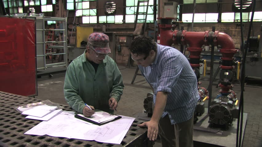 A factory worker and businessman sign documents in a factory
