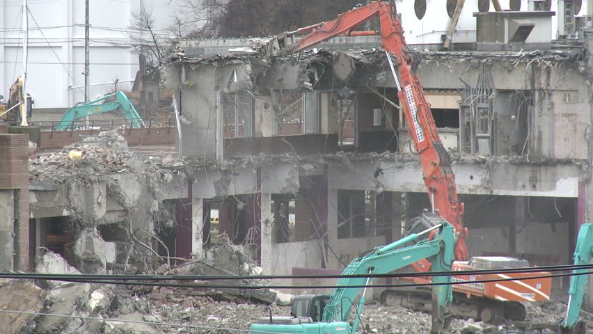 Japan Tsunami 1 Year On - Demolishing Damaged Building. Construction equipment works to demolish building in Onagawa city damaged by March 11th 2011 earthquake and tsunami in Japan.