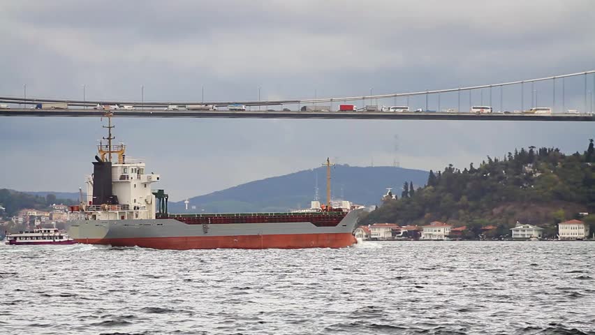 Bosporus Sea traffic with a cargo ship in Istanbul, Turkey. Transportation concept with a cargo ship sailing under busy bridge.
