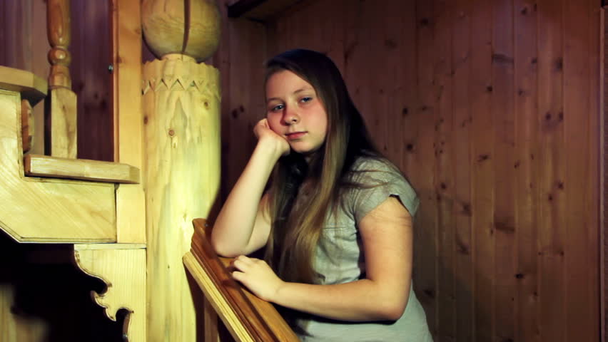 cute teenage girl stands and corrects hand their hair leaning on railing carved wooden stairs in house