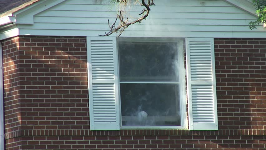 House fire.  Smoke seeping out of a window.  Close up.