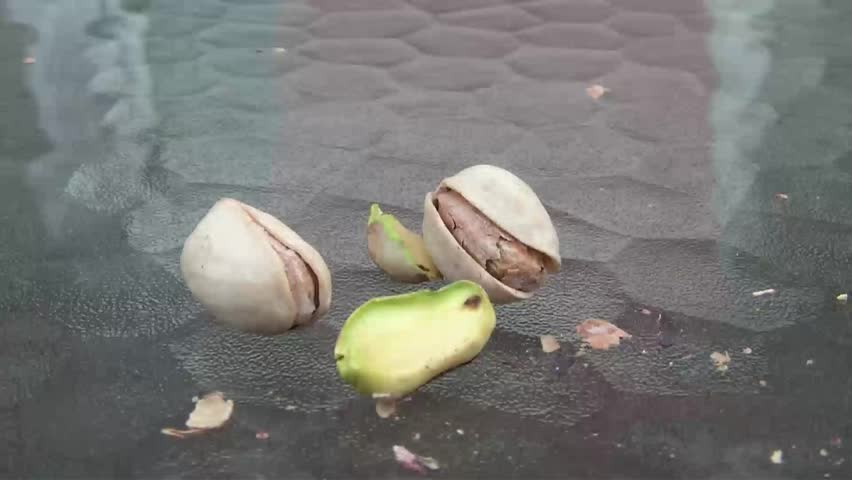 Opening pistachios close up on glass table and later picking some green nuts up to eat, outdoor summer lighting.
