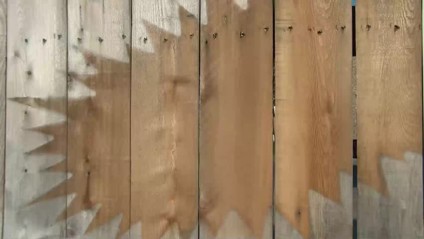 Raw brown wood on fence is naturally preserved from previous advertising signage leaving pointed cut out area inside of gray discolored wood.