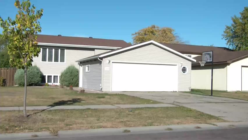 Green car pulls into driveway and awaits garage door to open to slowly cruise inside, in sunlight.
