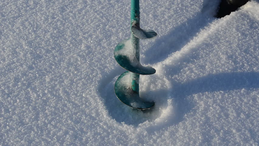 closeup of green metal steel drill drilling frozen snowy lake ice hole in winter. fisherman tool. fishing seasonal hobby.