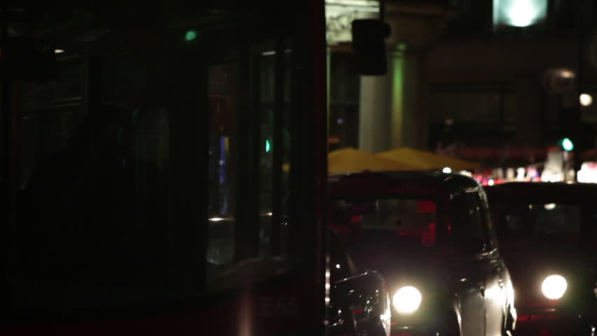 A stationary shot of busy evening street traffic in London. Buses and cars are passing and a building is in the background. 