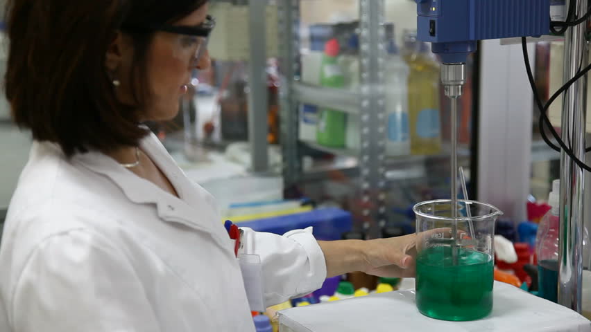 Female Scientist examining a beaker of fluid. Focus on the scientist.