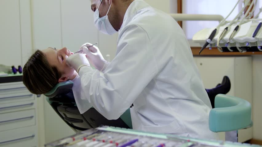 Close up of dental equipment in hospital with patient lying on exam chair and dentist working. Rack focus from tools to dentist