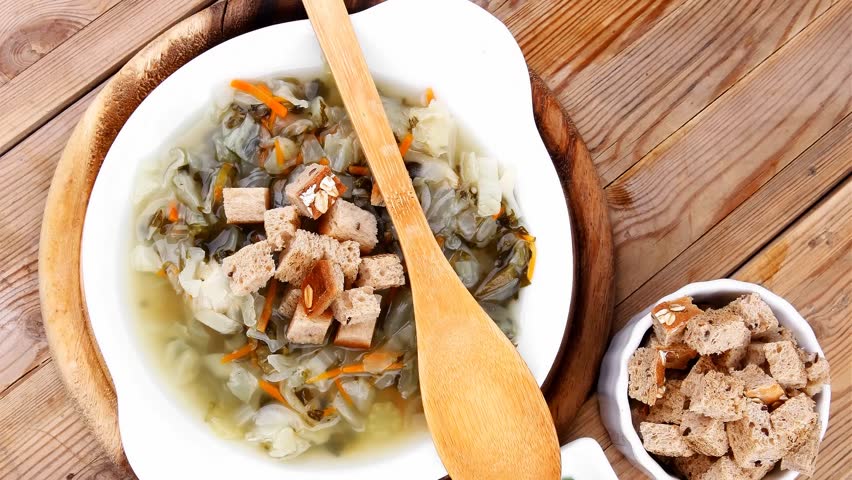 hot fresh diet vegetable soup with rye bread crackers over wood table on stand