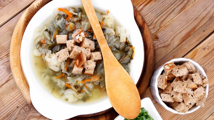 hot fresh diet vegetable soup with rye bread crackers over wood table on stand