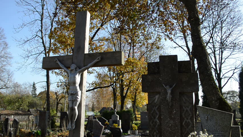 closeup of wooden cross with crucified jesus and stone monuments in rural autumn graveyard cemetery. death smell.