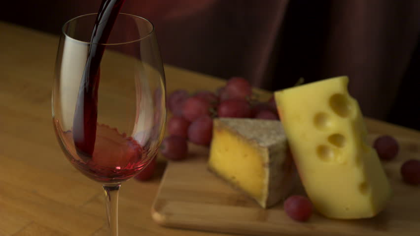 Pouring red wine into glass with grape and cheese shooting with a high speed camera.