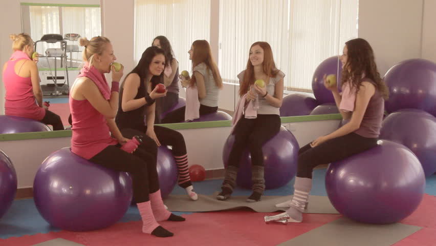 Beautiful sexy girls resting and eating apples after hard work out in fitness club. Healthy snack. 
