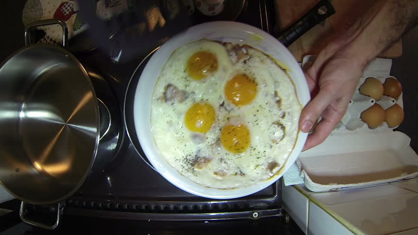 Fried Eggs and Bacon in a Pan.
Man takes out the eggs and bacon from the pan and serve them on a plate. HD1080p.