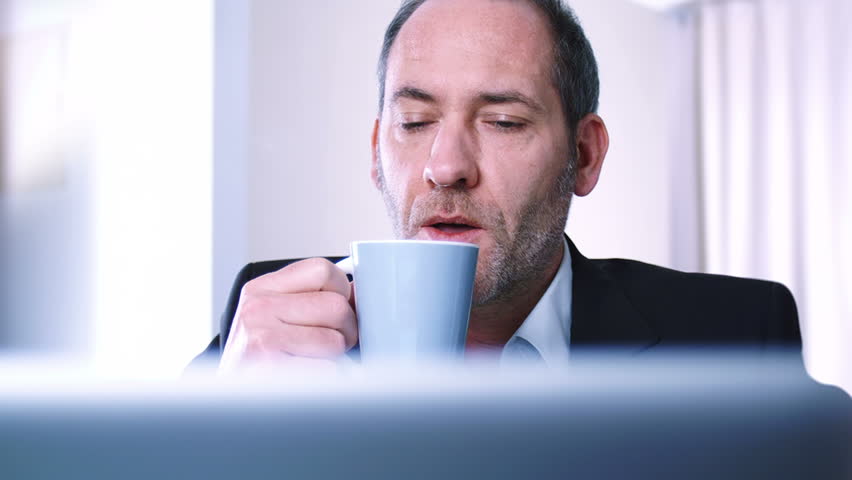 Businessman drinks coffe while watching the laptop screen - tracking shot