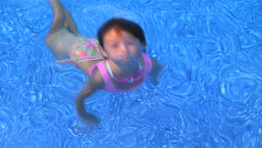 Little girl swimming underwater  in clear blue water and coming up smiling. 