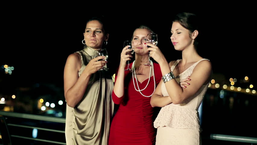 Three female friends enjoying night party on the terrace, crane shot
