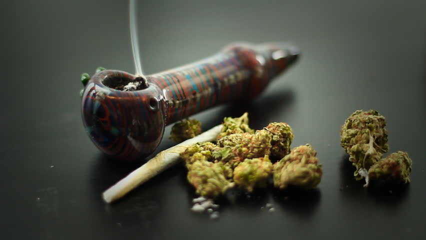 Marijuana Pipe Burning 1. A marijuana filled pipe smoking. More marijuana and a joint to the side.