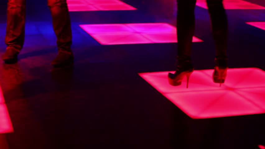 Three women and one man dance in night club, shown in motion with only legs visible