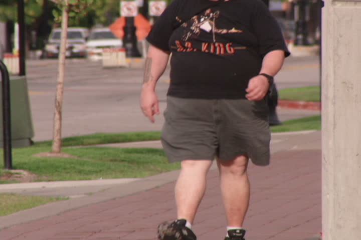 An overweight man walking down urban street.