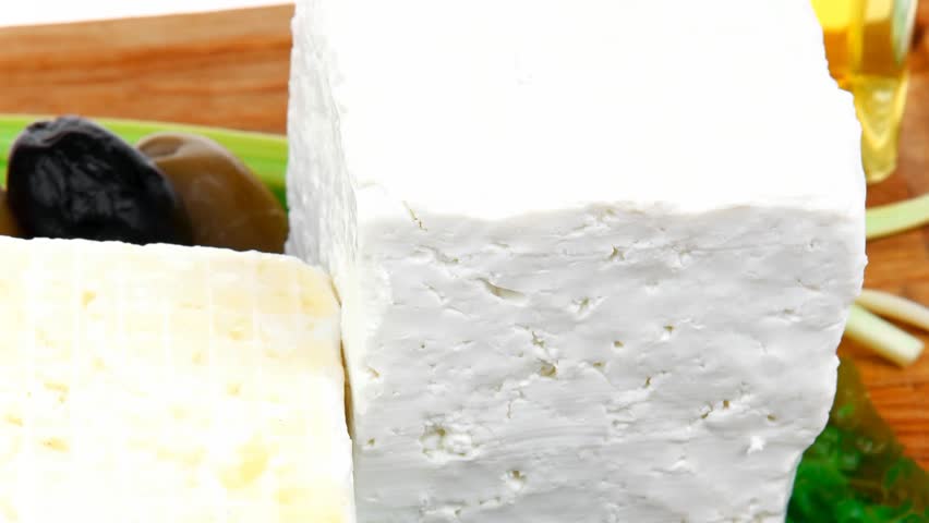 diet food : greek feta white cheese served on wooden plate with basil leaves red hot pepper black and green olives and olive oil isolated over white background