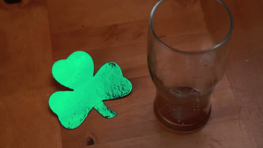 Hand putting down empty pint beside large shamrock on wooden surface