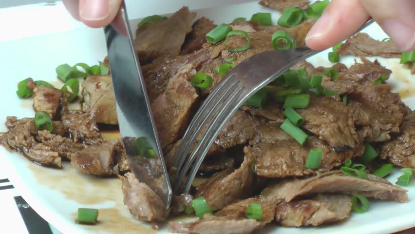 Delicious seared succulent slices of grilled steak served on a plate and about to be cut with a knife and fork.