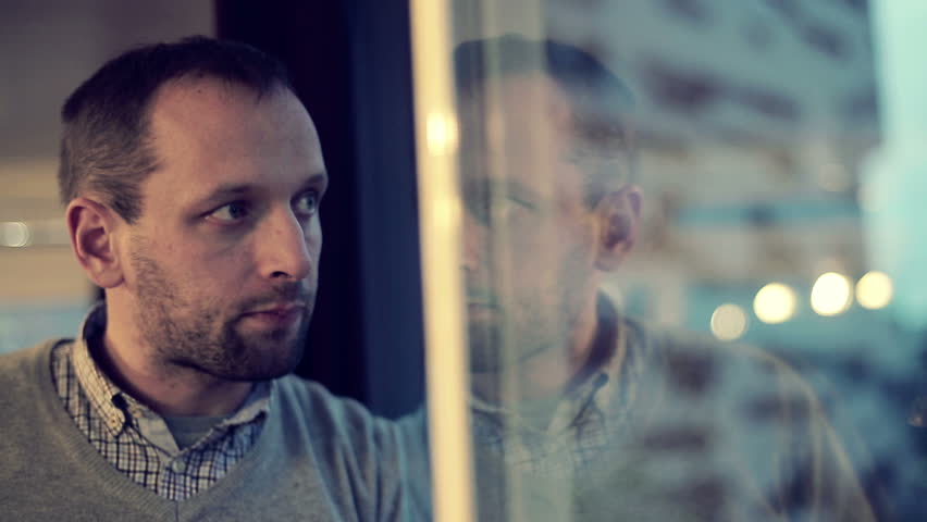 Sad, depressed man drinking tea by the window in home
