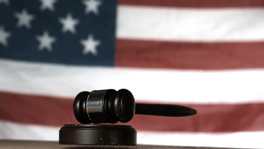 Gavel dropping onto sounding block with american flag in background in slow motion