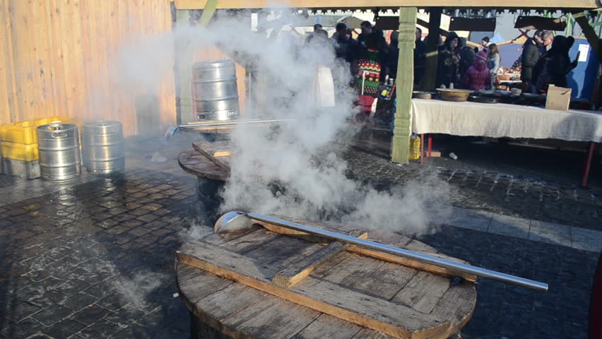 People buy hot drink wine boil in huge pots and smoke vapour rise in spring outside market fair.