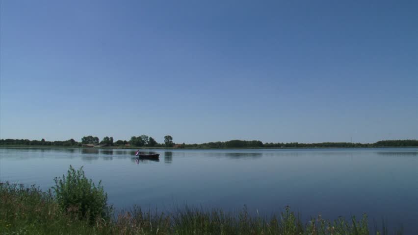 Small fishing boat on quiet blue lake + pan artificial Lake Oldambtmeer, Groningen, The Netherlands.