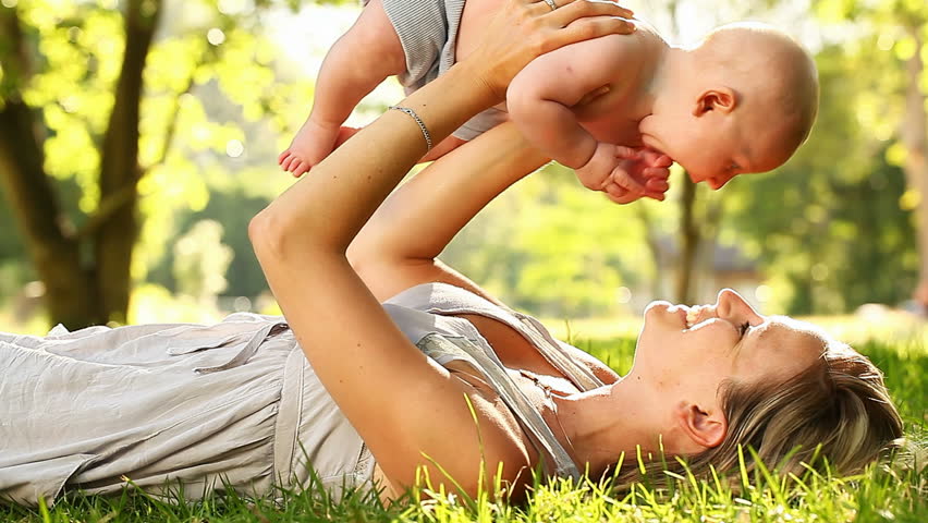 Young Mother Holding Her baby son aloft in park or garden