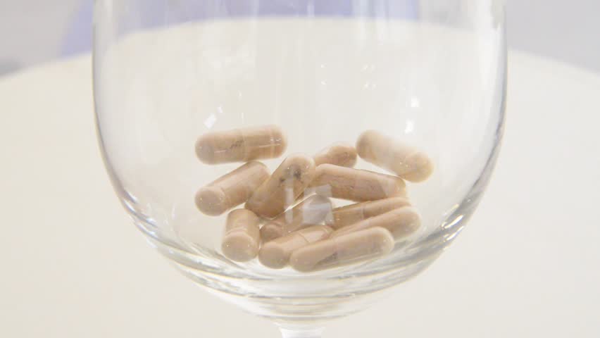 Herbal medicine capsules dropping into a glass.