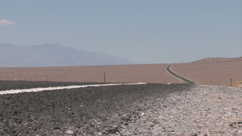 Car in the background on a Highway winding through the Desert with heat haze on the pavement
