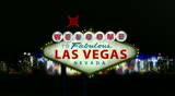 Camera Pans down to show the Welcome to Las Vegas sign with a blurred city in the background with lots of neon lights and energy.