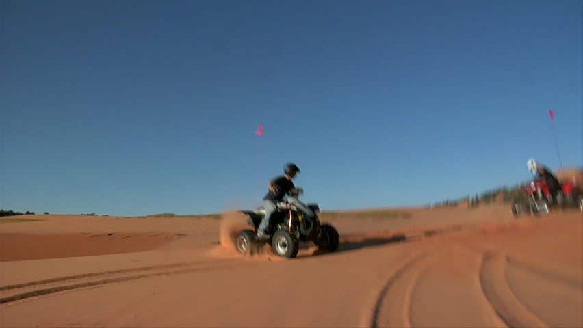 slow-motion ATV riders kick up sand