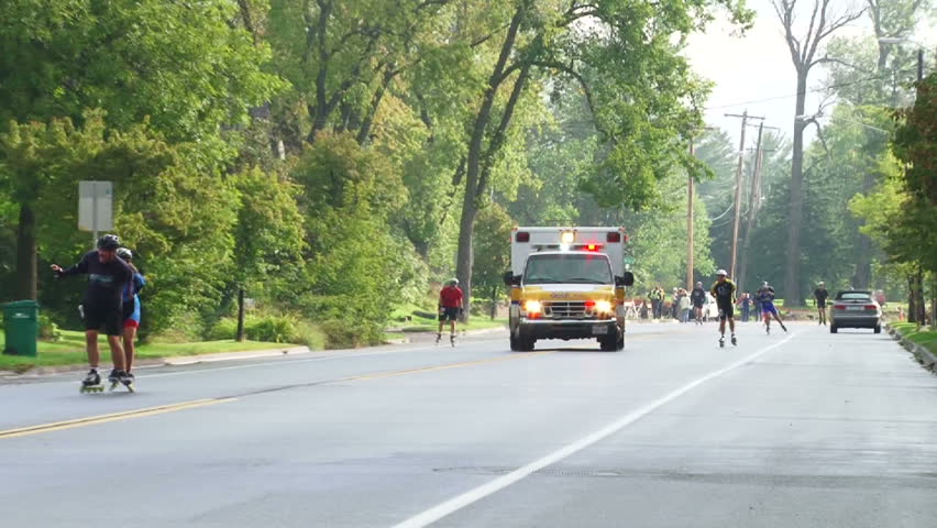 DULUTH, MINNESOTA, CIRCA 2012: Ambulance with lights flashing speeds by camera in emergency during street marathon, with sound.
