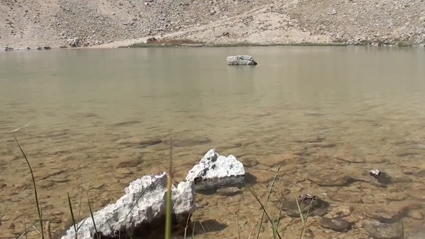 Water of crater lake, stones in it, reflection of surface