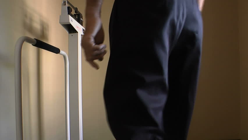 Man steps on medical scale, moves bars until balanced, checks weight at doctorâs office. 1080p
