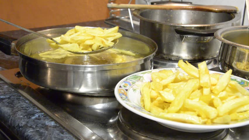 Stirring French Fries With wooden Spatula in fryer pan closeup. Boiling in oil.