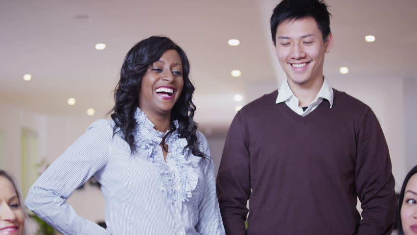 An attractive and enthusiastic mixed ethnicity team of young professionals enjoy a light hearted moment of laughter together while they are at work. In slow motion.