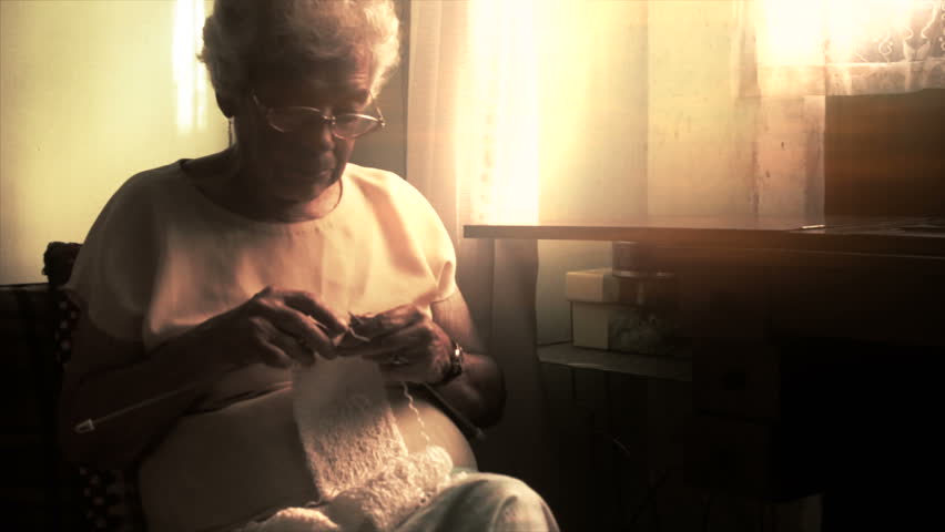 Older woman knitting a scarf with needles at home 