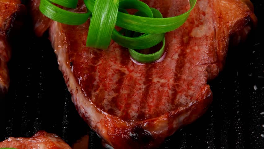 fresh grilled bloody beef steaks on black grill plate with green leaves isolated on white background