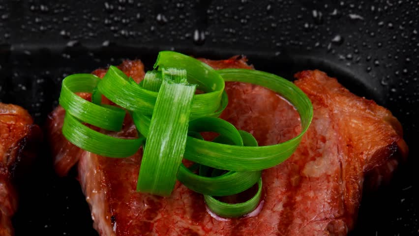 fresh grilled bloody beef steaks on black grill plate with green leaves isolated on white background