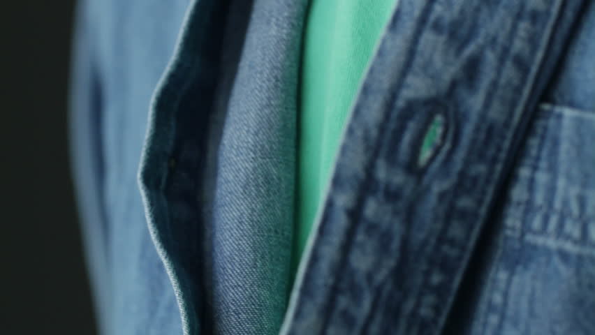 Hands doing up the buttons on a denim shirt. POV shot with a macro lens and shallow depth of field.
