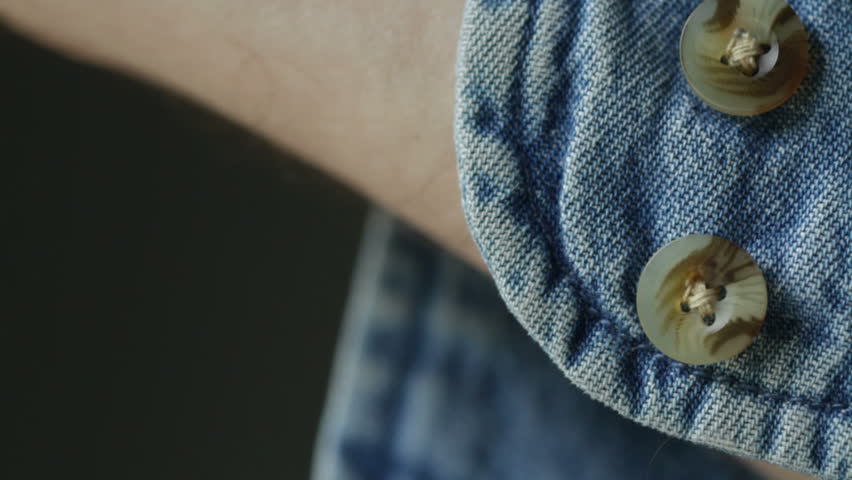 Close shot of hand doing up the button on the cuff of a denim shirt. Recorded with macro lens and very shallow depth of field.