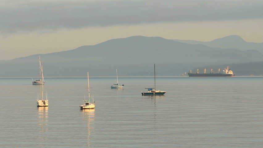 Sailboat Motoring at Dawn, Vancouver. A sailboat motors past anchored sailboats at dawn in English Bay, Vancouver, British Columbia, Canada.